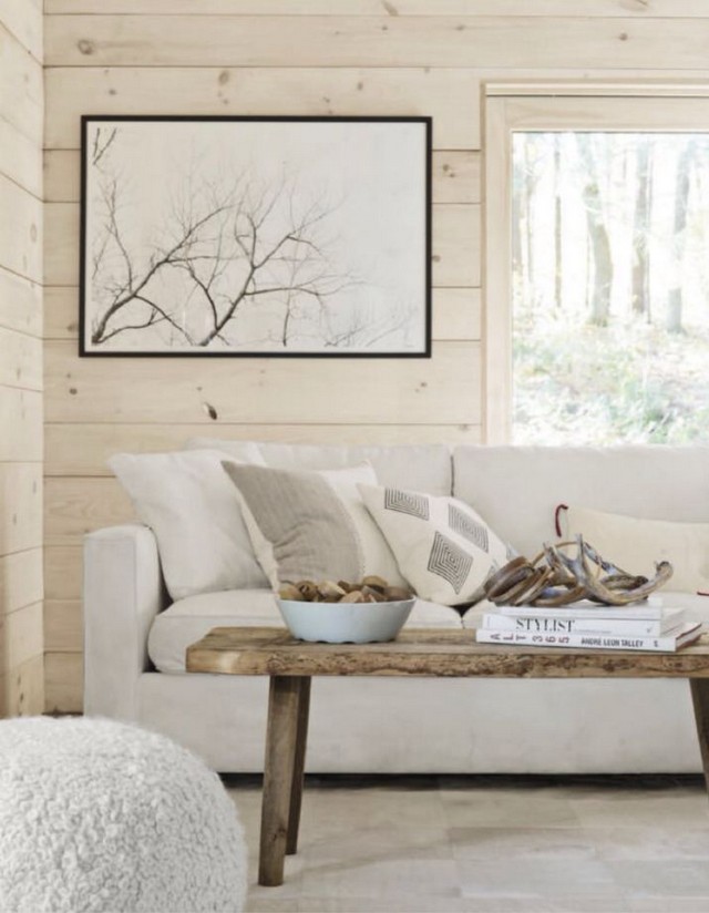 In this white living room there’s a cabin board sofa and CB2 pouf ...